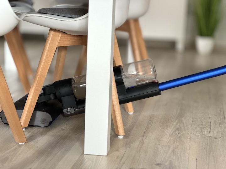 Dyson reinigt unter einem Tisch zwischen Stuehlen